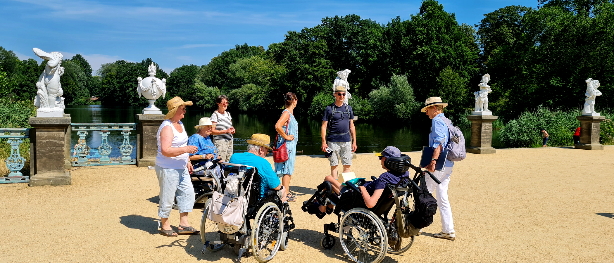 Foto: Eine Reisegruppe mit Rollstuhlnutzenden im Charlottenburger Schlosspark an einem Sommertag