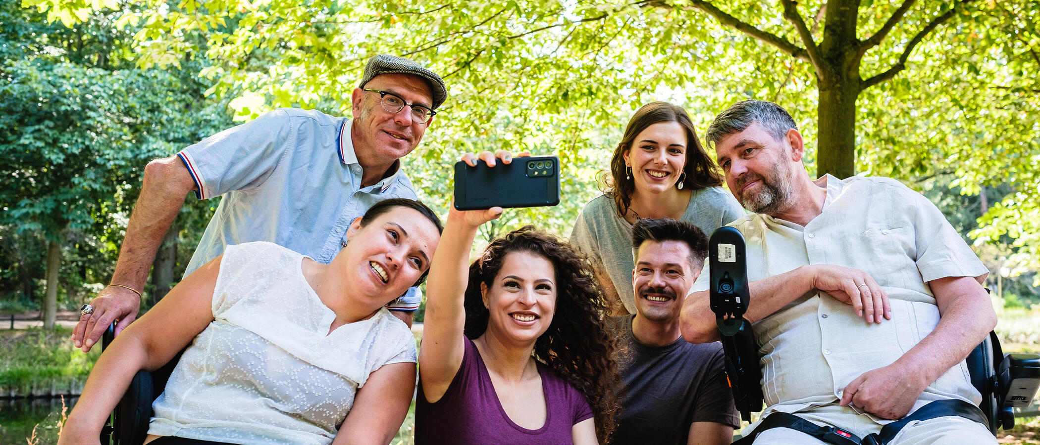 Eine Gruppe Menschen mit und ohne Behinderung macht in einer Grünanlage ein Gruppen-Selfie.
