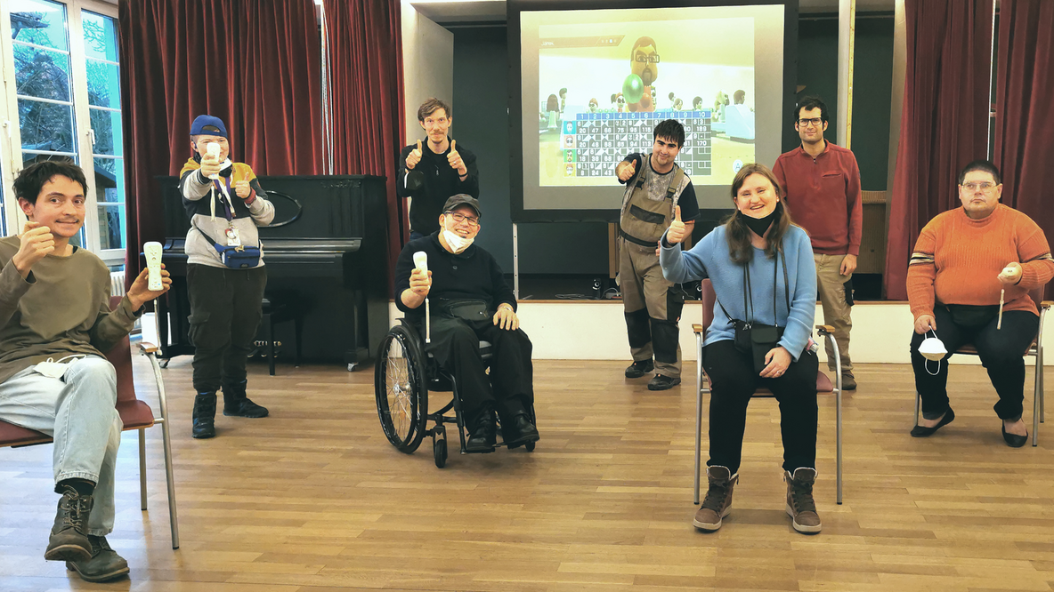 Foto: Eine Gruppe junger Menschen mit den Wii-Contzrollern in der Hand, im Hintergrund das Spiel Bowling projiziert auf Leinwand