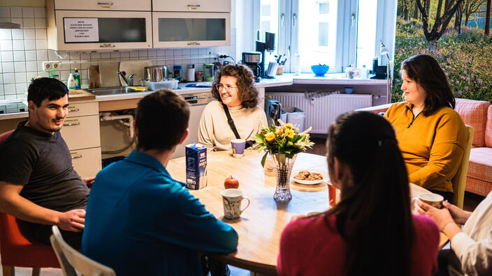 Mehrere Personen sitzen in ihrer WG an einem runden Tisch und unterhalten sich.