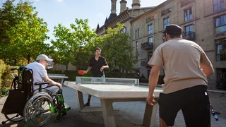 Drei Männer, davon einer im Rollstuhl, spielen Tischtennis vor dem WMI Pankow.