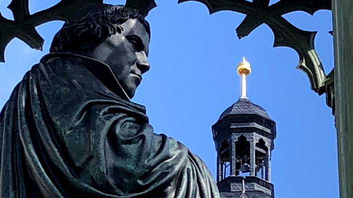 Foto: Das Martin Luther-Denkmal in Wittenberg in Nahaufnahme, im Hintergrund der Turm der Schlosskirche