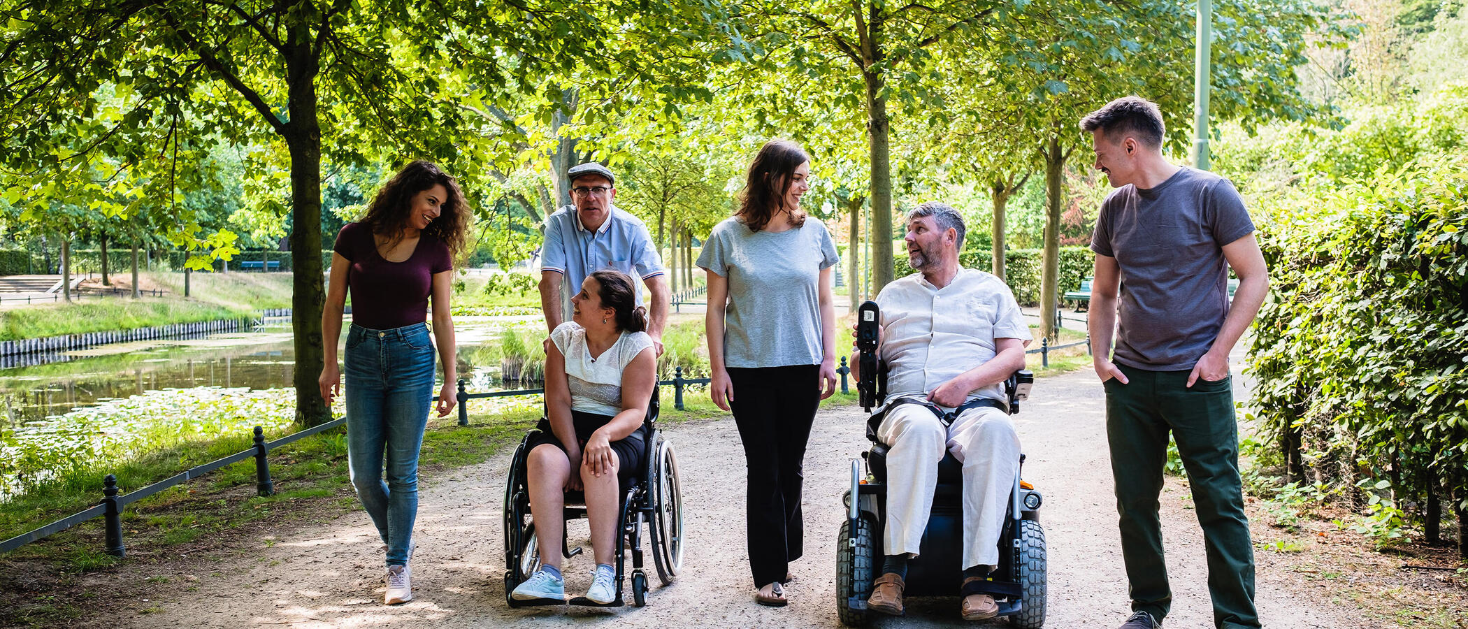 Eine Gruppe Menschen mit und ohne Behinderung macht einen gemeinsamen Spaziergang in einer Grünanlage.