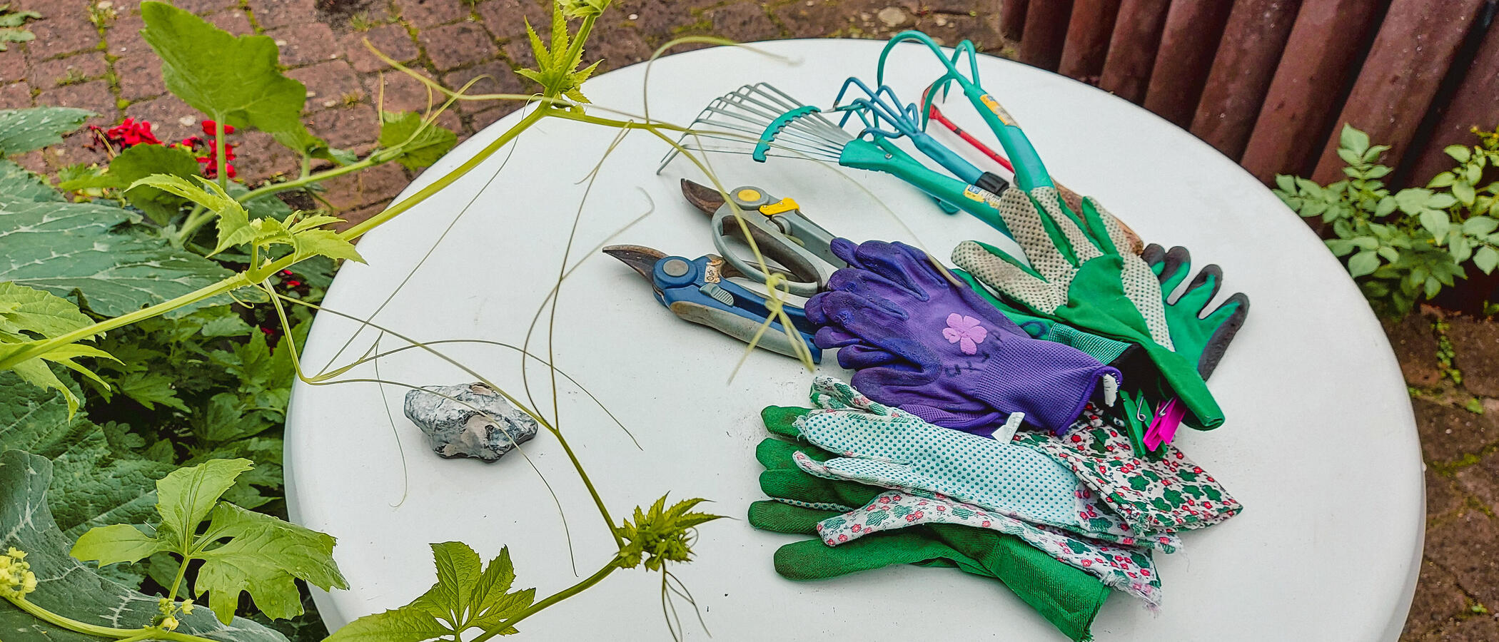 Foto: Gartenwerkzeuge und Arbeitshandschuhe auf einem runden, weißen  Gartentisch