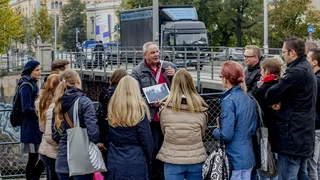 Foto: Dieter Bichler, ein Mann im fortgeschrittenen Lebensalter, referiert auf einer Berliner Brücke vor einer gemischten Gruppe jüngerer Menschen