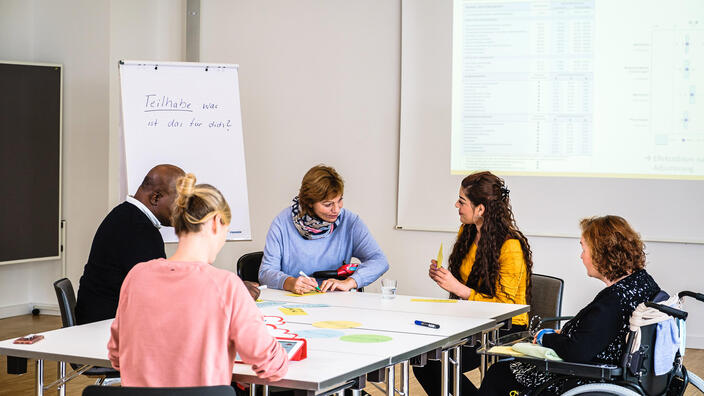Mehrere Personen Sitzen am Tisch und beraten sich. 