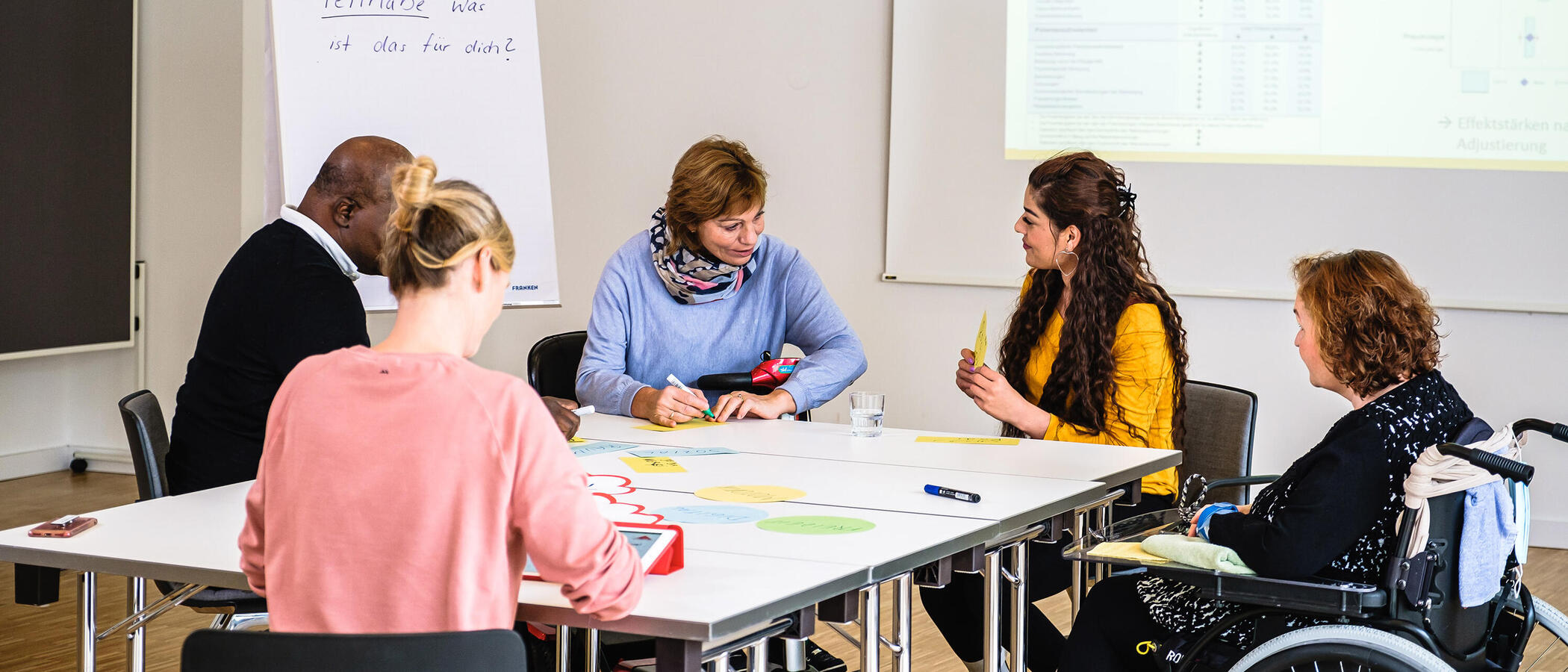 Mehrere Personen Sitzen am Tisch und beraten sich. 