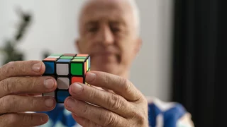 Foto: Ein älterer Mann, unscharf im Hintergrund, hält einen Rubik-Cube in den Händen