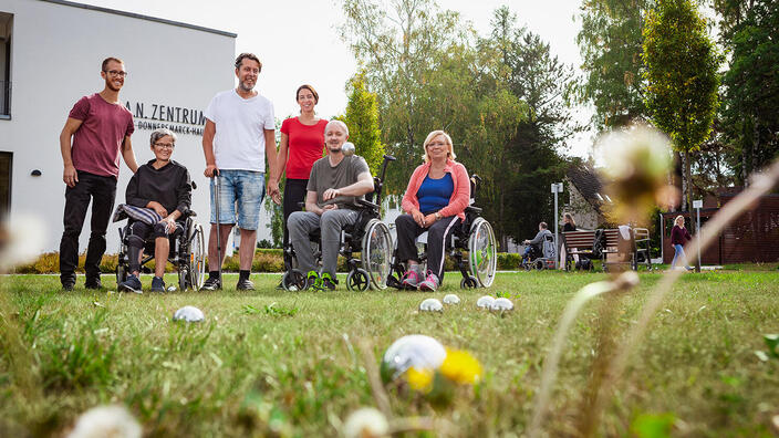 Eine Gruppe Rehabiltandinnen und Rehabilitanden spielt auf der Wiese vor dem P.A.N. Zentrum Boccia.