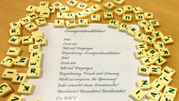 Foto: Ein Gedicht auf Papier, umrahmt von Scrabble-Buchstaben