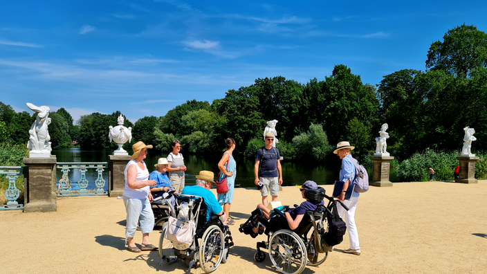 Foto: Eine Reisegruppe mit Rollstuhlnutzenden im Charlottenburger Schlosspark an einem Sommertag