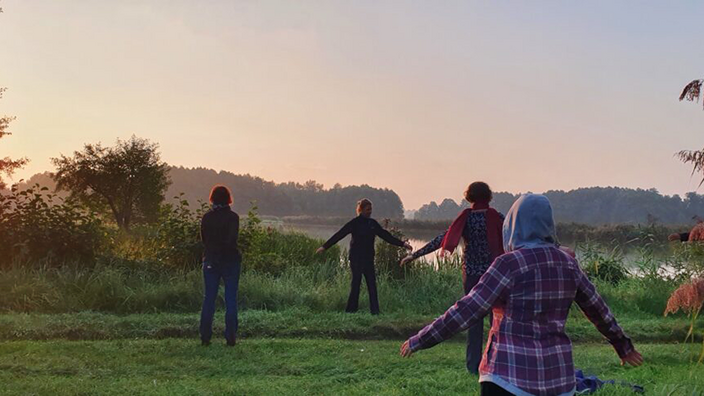 Foto: Eine Gruppe macht Entspannungsübungen in der Natur bei Sonnenaufgang