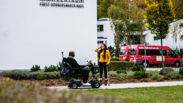 Ein Mann im Elektrorollstuhl und eine Frau mit Gehhilfe stehen vor dem P.A.N. Zentrum und unterhalten sich.