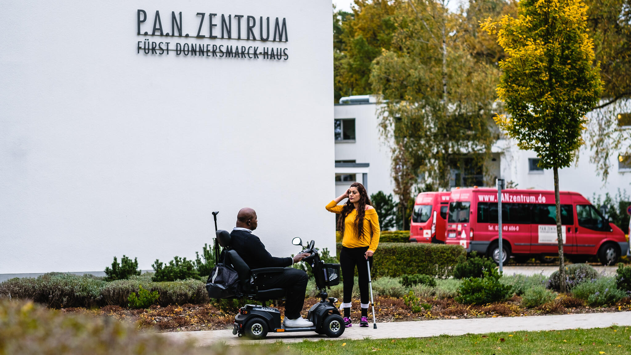 Ein Mann im Elektrorollstuhl und eine Frau mit Gehhilfe stehen vor dem P.A.N. Zentrum und unterhalten sich.