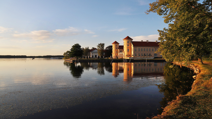 Foto: Das Schloss Rheinsberg vom See bettrachtet bei Sonnenuntergang. Foto von Udo Urban.