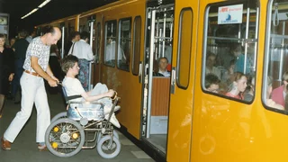 Historisches Foto aus den 80er/90er Jahren: ein Mann hilft einem Rollstuhlfahrer beim Einsteigen in die Berliner U-Bahn.