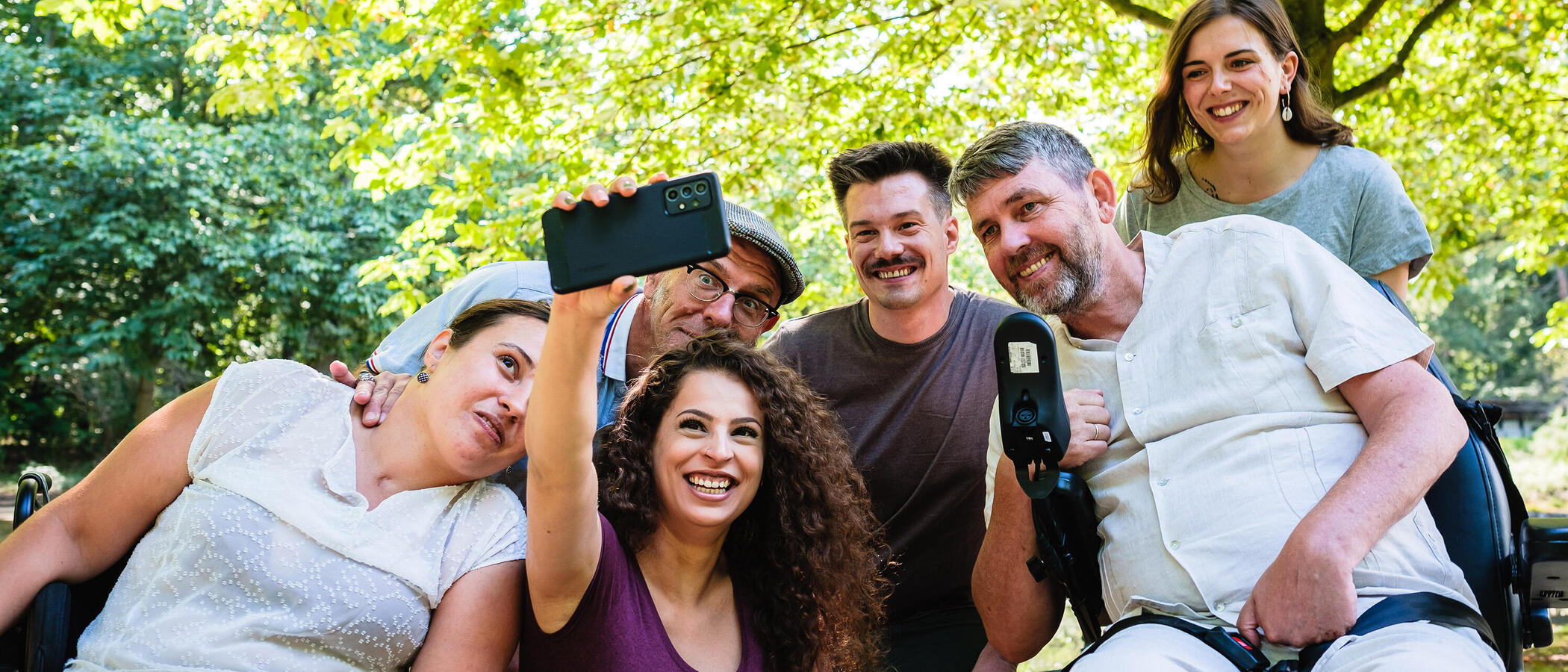 Eine Gruppe Menschen mit und ohne Behinderung macht in einer Grünanlage ein Gruppen-Selfie.