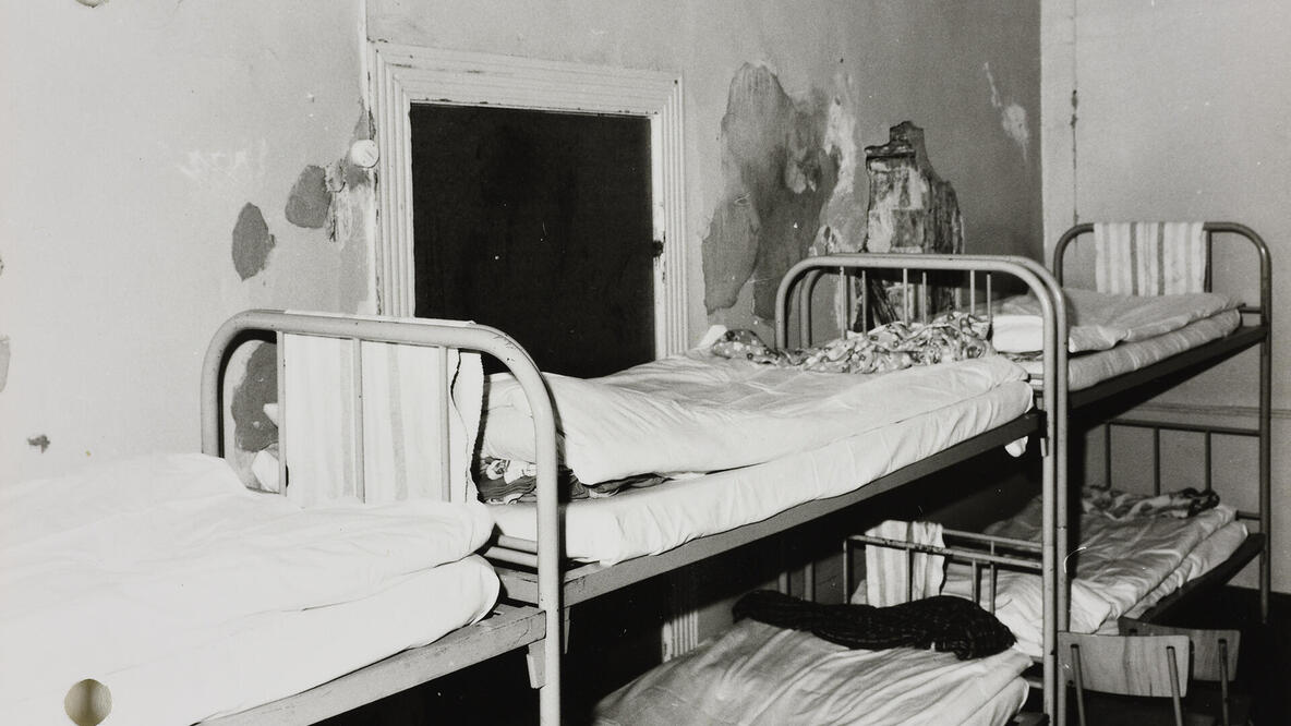 Historisches Foto: Etagenbetten in einem Zimmer eines Jugendheims in der DDR. Von den Wänden bröckelt stellenweise die Farbe.