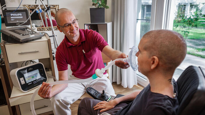 Eine Situation im Bereich Rehabilitative außerklinische Intensivpflege: Ein Mitarbeiter unterstützt einen Klienten mit dem Beatmungsgerät.
