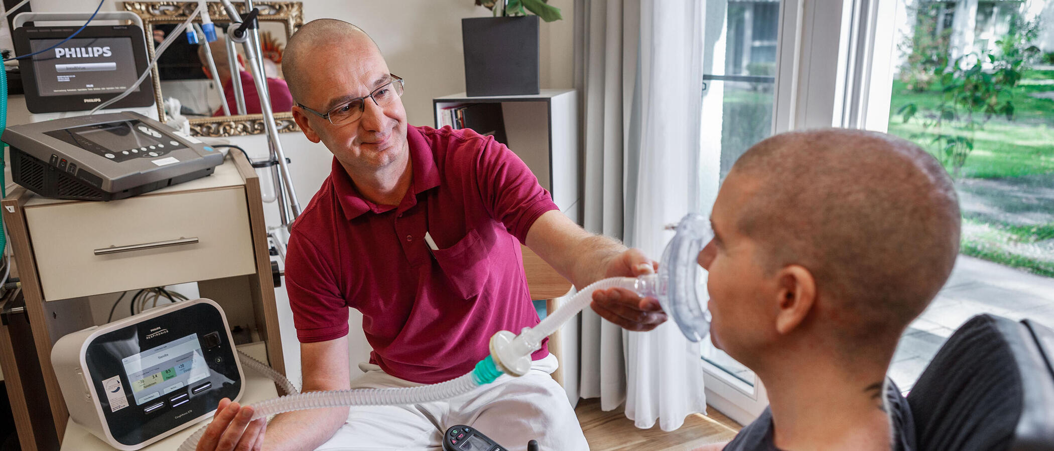 Eine Situation im Bereich Rehabilitative außerklinische Intensivpflege: Ein Mitarbeiter unterstützt einen Klienten mit dem Beatmungsgerät.