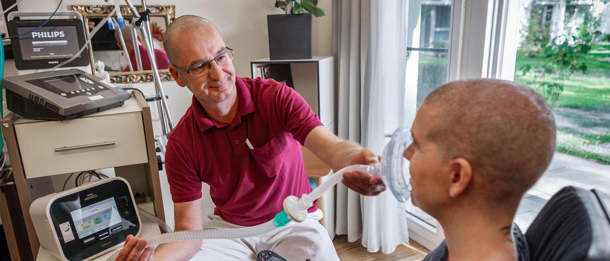 Eine Situation im Bereich Rehabilitative außerklinische Intensivpflege: Ein Mitarbeiter unterstützt einen Klienten mit dem Beatmungsgerät.