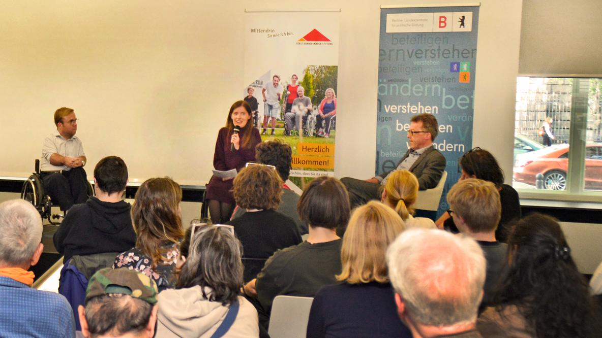 Foto: Podiumsdiskussion Denkstile, im Vordergrund Hinterköpfe des Publikums, auf der Bühne Moderatorin Adina Hermann und Podiusmgäste Dr. Leopold Rupp (links) und Prof. Dr. Cornelius Borck (sitzend rechts)